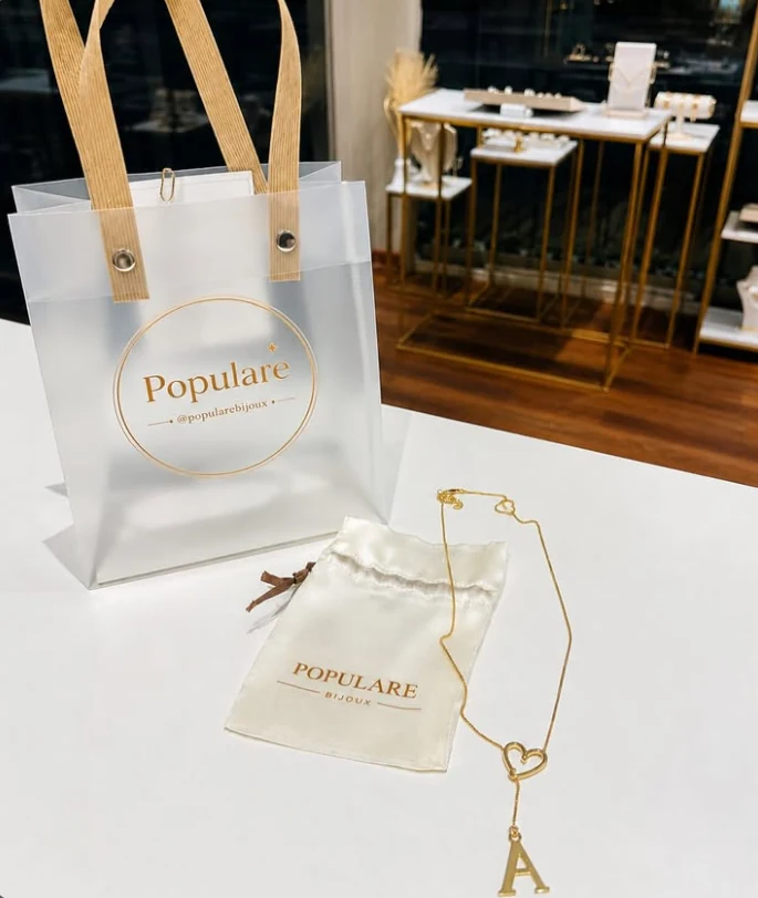 Colar com pingente e embalagens da Populare Bijoux sobre uma mesa.